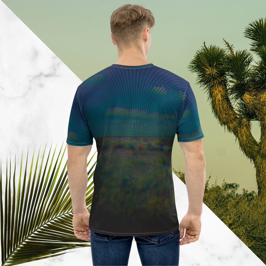Full color all over print graphic tee shirt with image of a desert and green desert plants and blue sky with clouds above the horizon overlayed with rgb distortion and psychedelic lines graphics fanning outward towards the top