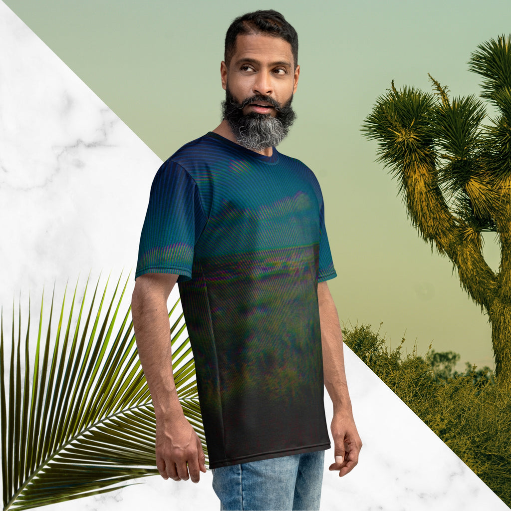 Full color all over print graphic tee shirt with image of a desert and green desert plants and blue sky with clouds above the horizon overlayed with rgb distortion and psychedelic lines graphics fanning outward towards the top