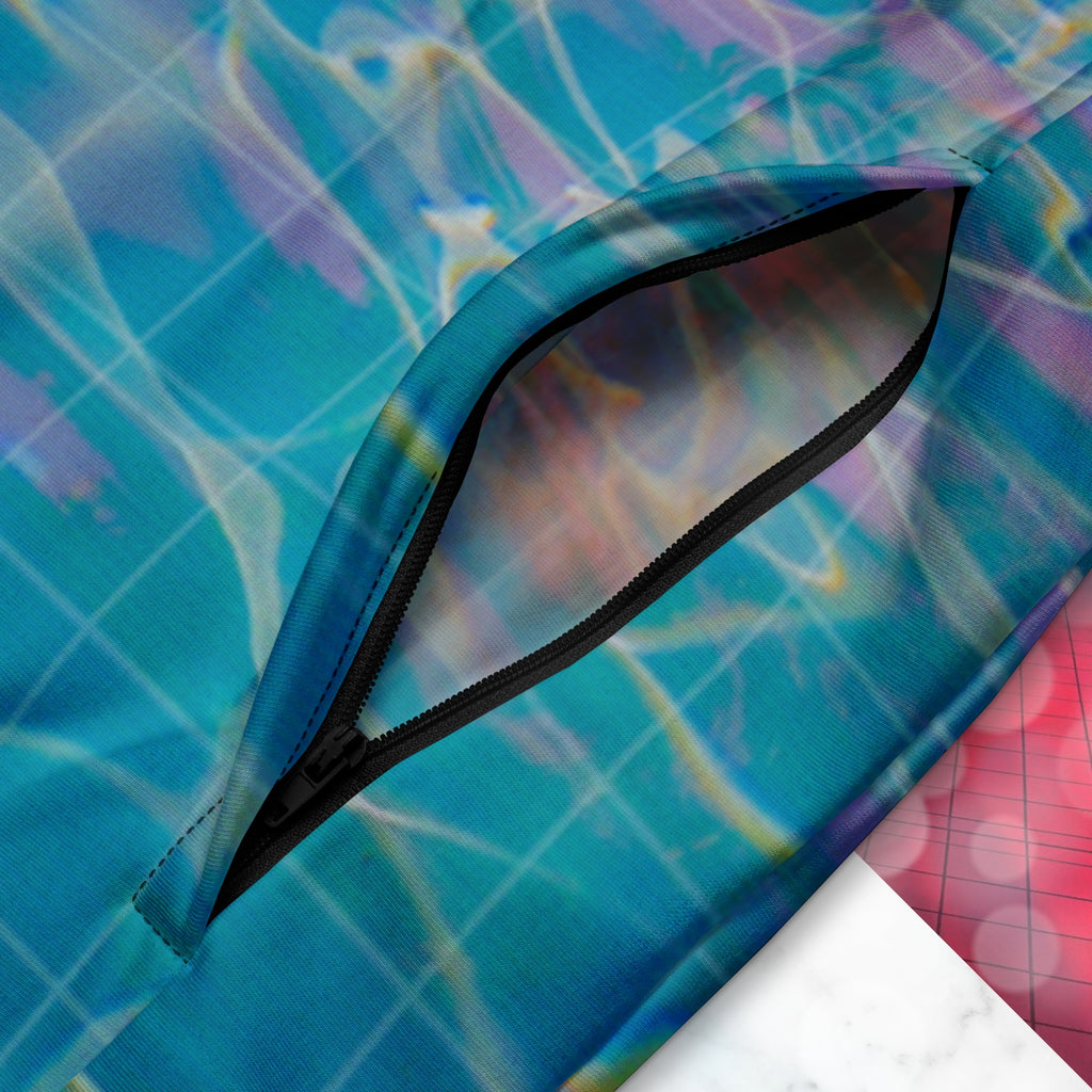 Closup of pocket zipper on multicolored all over print track jacket depicting blue water reflecting the colors of the sunset in oranges and pinks intensifying towards the top overlayed with a transparent thin white grid with tropical plant silhouettes of tropical plants creating stripe effects on sleeves with Neon Pools vaporwave sun emblem on left chest area