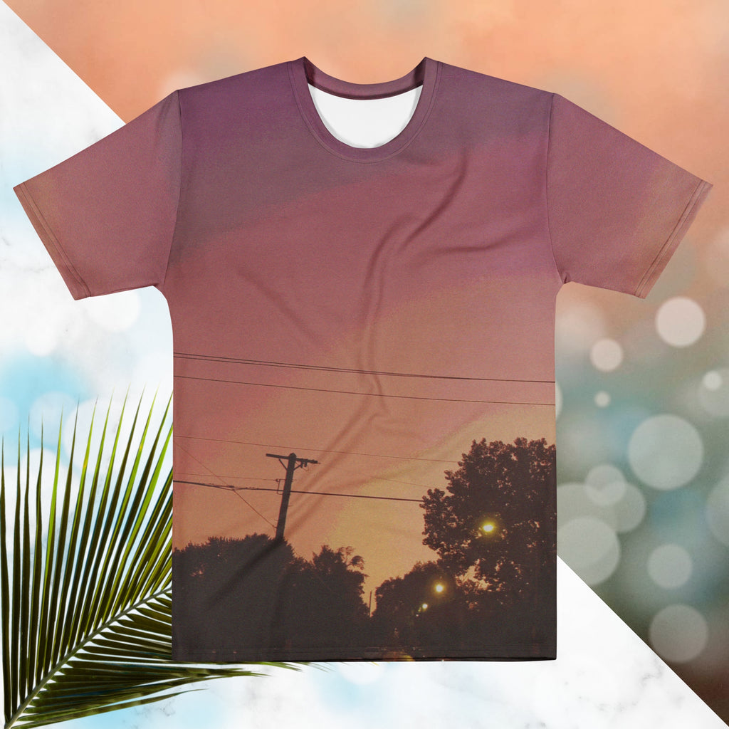 Multicolored all over print graphic t-shirt depicting a sunset with concentric layers of purple, red, orange and yellow with a foreground of trees, street lights, telephone lines and a city street with detailed vhs effects