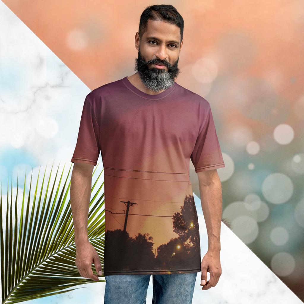 Multicolored all over print graphic t-shirt depicting a sunset with concentric layers of purple, red, orange and yellow with a foreground of trees, street lights, telephone lines and a city street with detailed vhs effects
