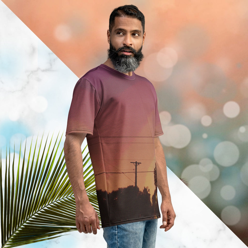 Multicolored all over print graphic t-shirt depicting a sunset with concentric layers of purple, red, orange and yellow with a foreground of trees, street lights, telephone lines and a city street with detailed vhs effects