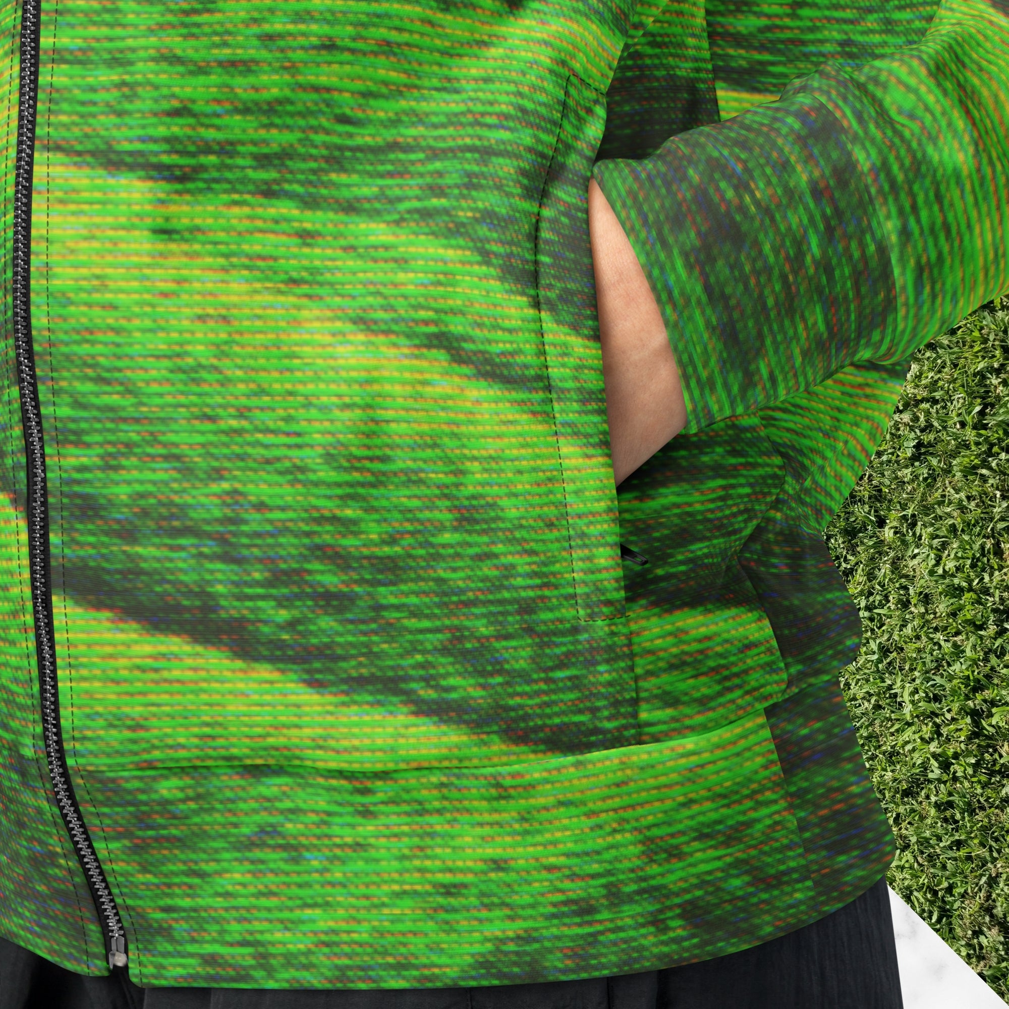 Closeup of pocket on primarily green and black full color all over print track jacket depicting grass covered green rolling hills and their shadows overlayed with detailed v h s and retro t v distortion with a green and blue Neon Pools vaporwave sun and waves emblem on the left chest