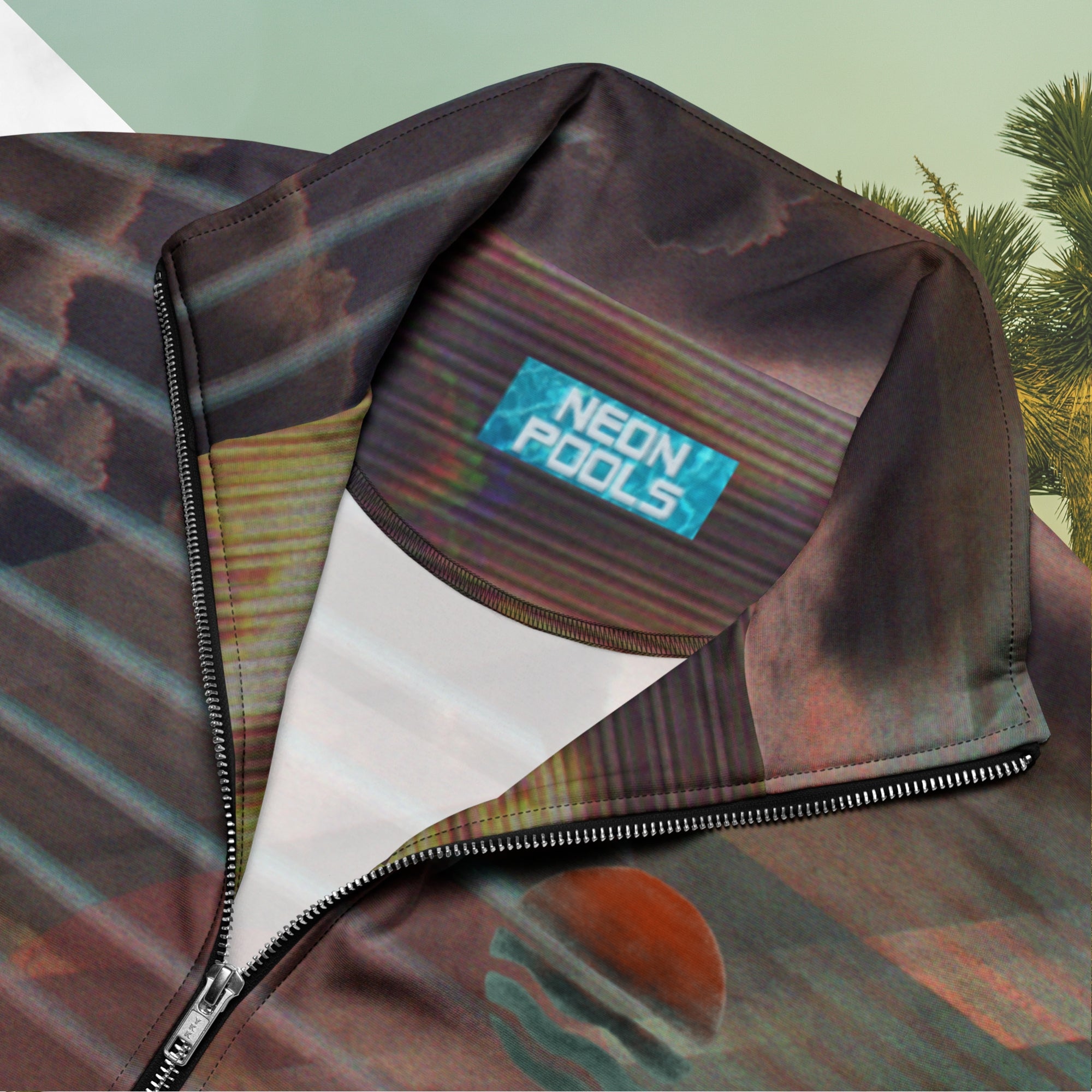 Close up of neckline and neon pools logo and insignia on full color all over print track jacket with retro ocean sunset with shimmering water photo overlayed with transparent stripes and graphic shapes in a 1980s memphis design style partial stripes and a transparent vaporwave broken sun in coral tone neon pools broken sun and waves logo emblem at left chest