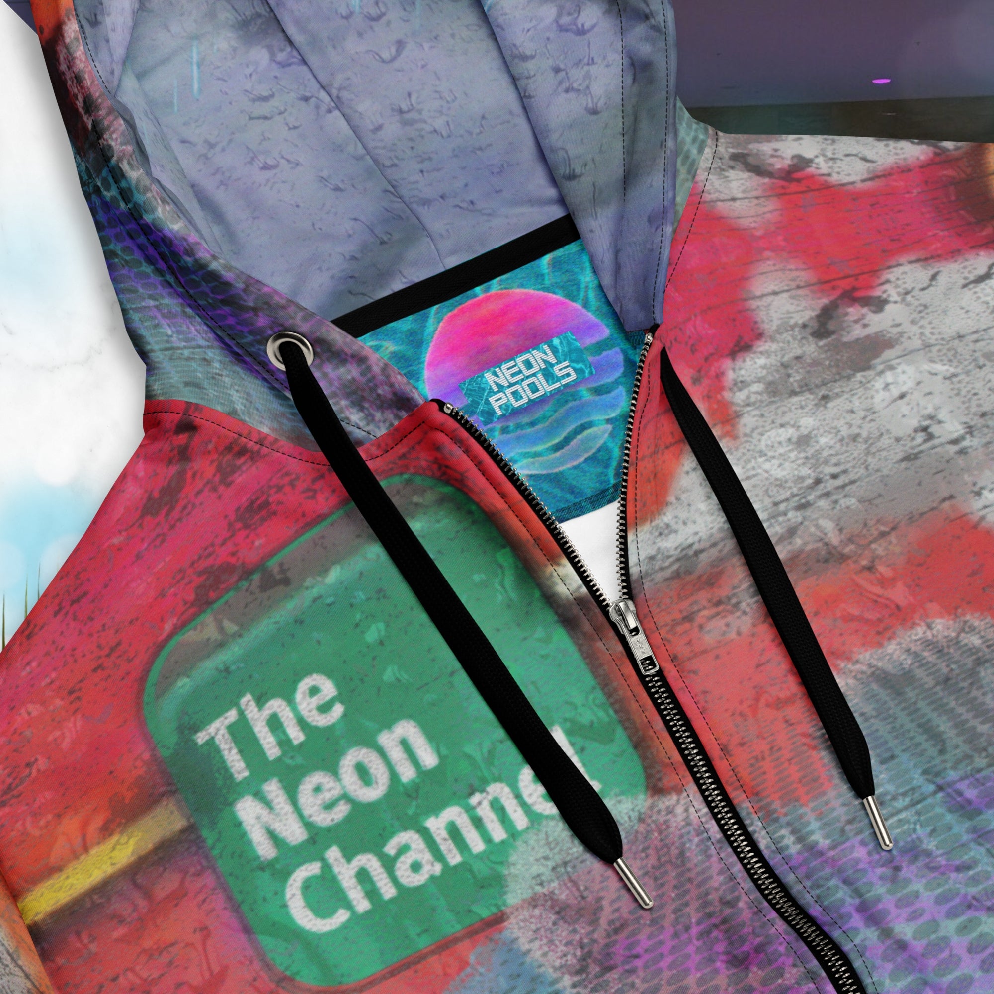 Closeup of neck line and Neon Pools insignia inner label patch on vibrant multicolored all over print zip hoodie with retro tv weather broadcast graphics featuring a logo that says The Neon Channel and the words tropical update teal and purple retro zigzag tropical sunset in brilliant oranges and reds with clouds 90s distortion blue dots graphics